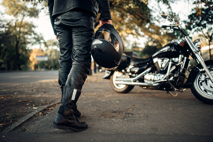 Motorcyclist with helmet in hand goes to his chopper, back view. Vintage bike, biker and his motorcycle, freedom lifestyle, biking